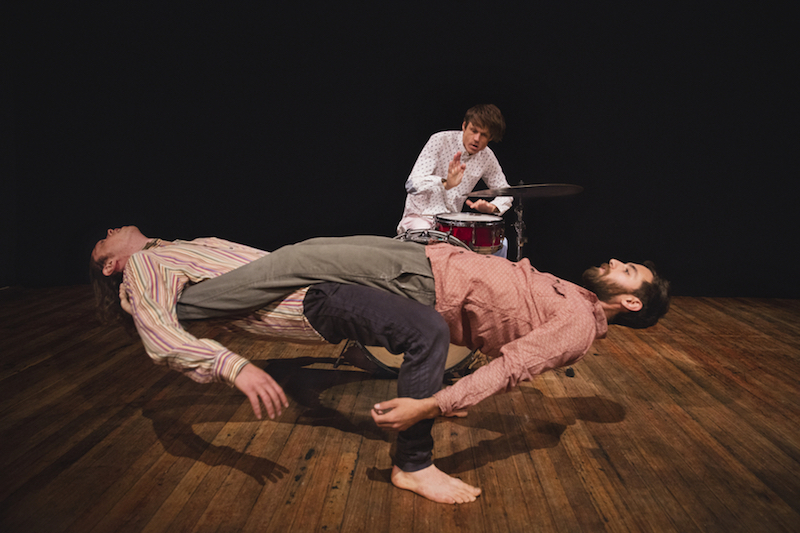 Two men hinge back. Their bodies are straight as a board. The drummer is in the background.